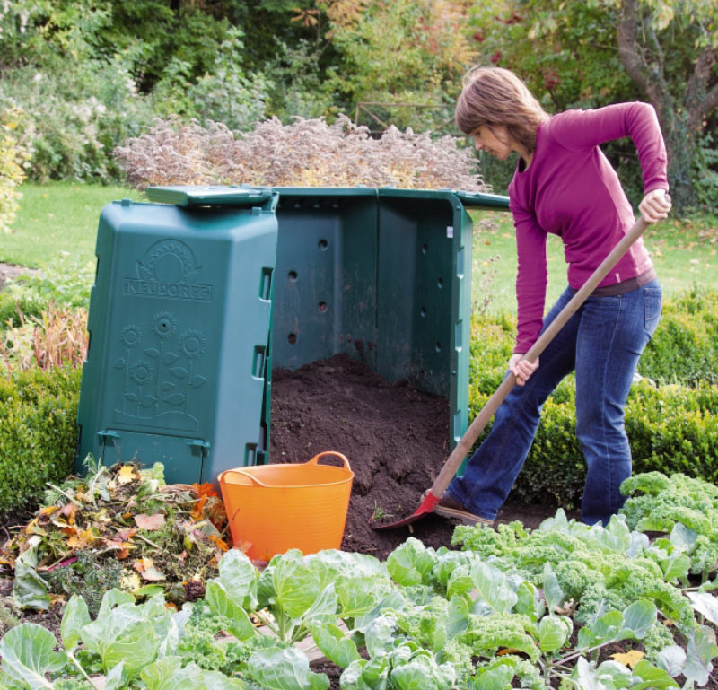 Frau entnimmt fertigen Kompost aus dem geöffneten Neudorff Thermokomposter