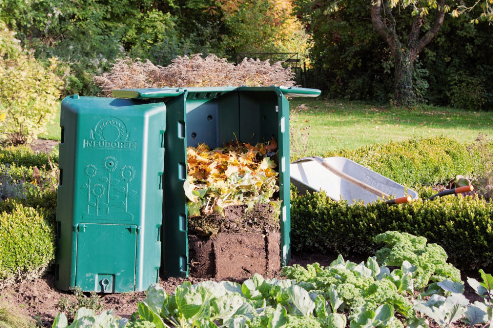 Geöffneter Thermokomposter mit verschiedenen Schichten aus Gartenabfällen, Laub und Humus