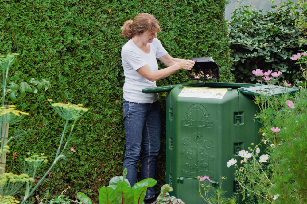 Frau entleert Küchenabfälle in den Komposter